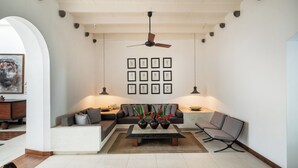 Een moderne woonkamer met een bank, salontafel en twee stoelen. Er hangen fotolijstjes aan de muur en er is een plafondventilator.