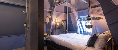 A bedroom with a bed, a shower, and a hanging light fixture.
