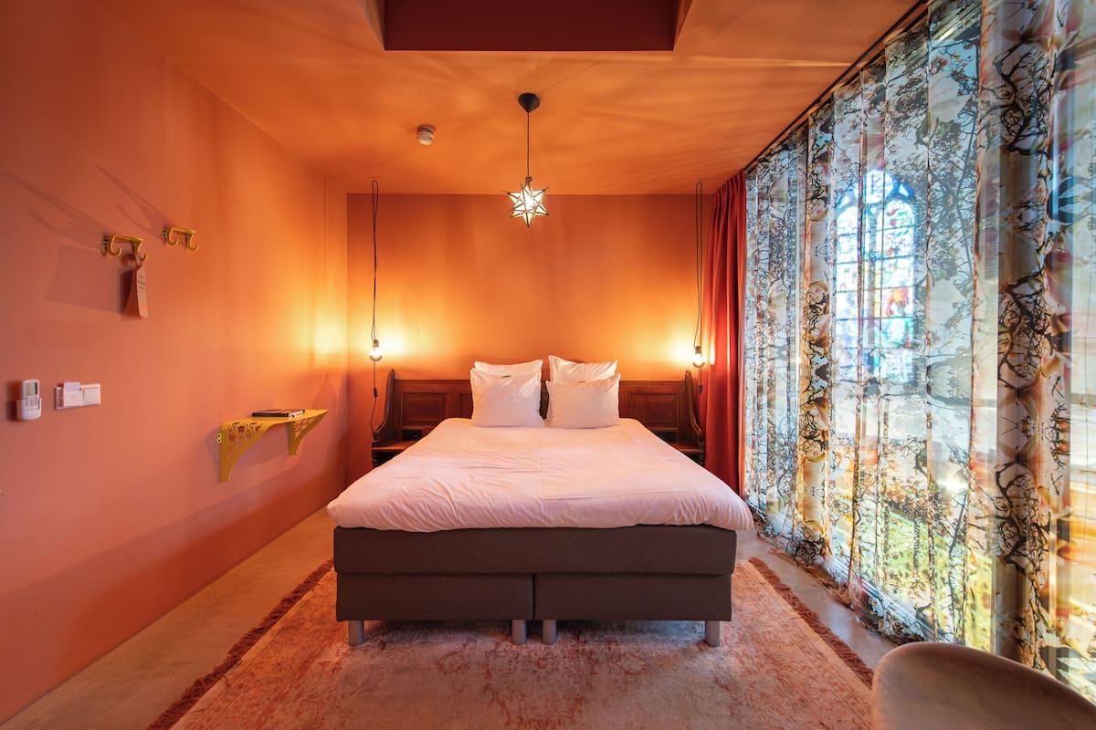 A bedroom with a large bed, a hanging star-shaped light fixture, a nightstand, and a window with patterned curtains.