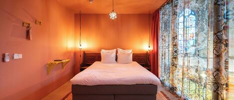 A bedroom with a large bed, a hanging star-shaped light fixture, a nightstand, and a window with patterned curtains.