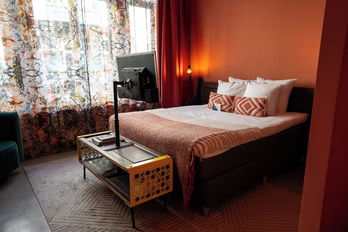 A hotel room with a bed, a desk, and a window with curtains.