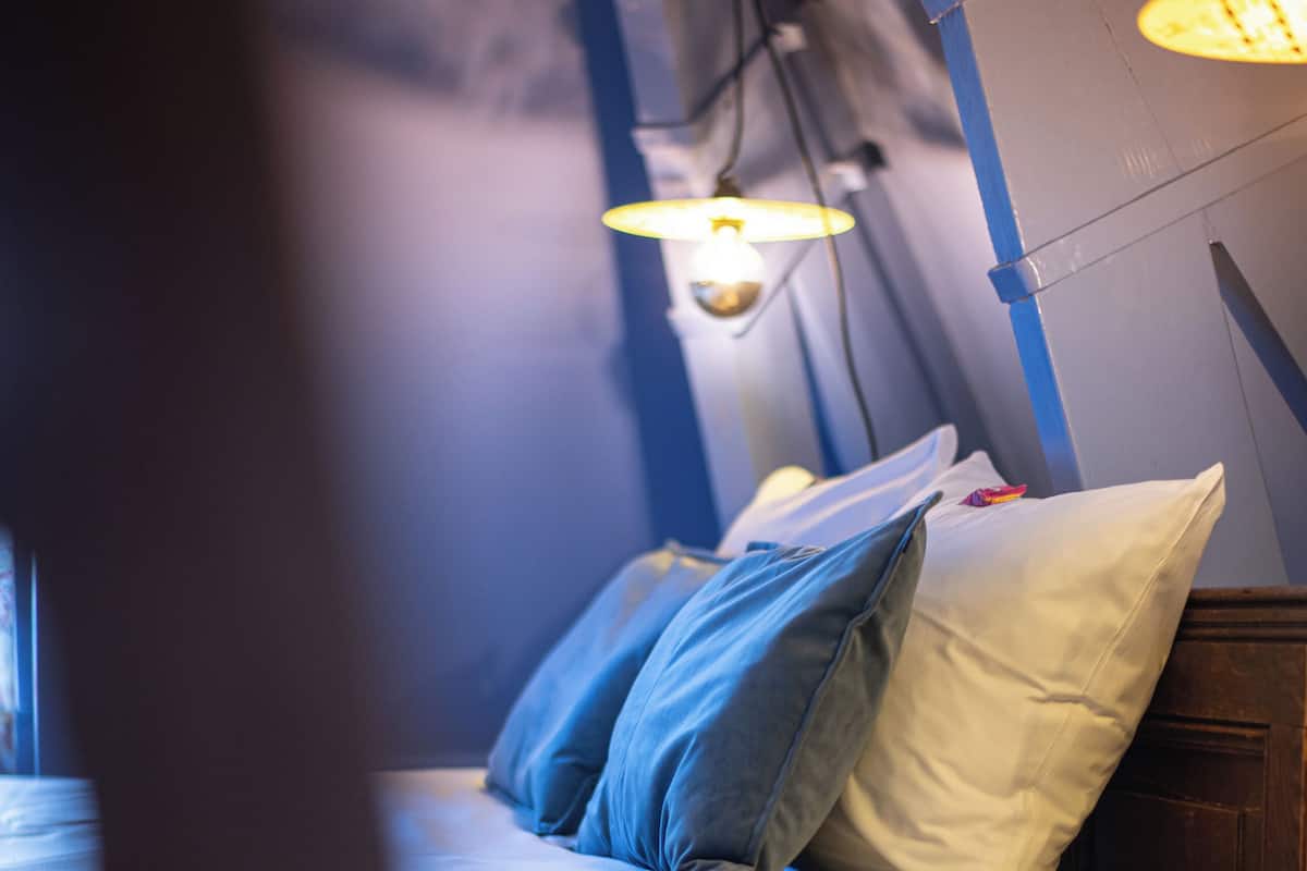 A bed with pillows and a lamp in a room with blue walls and a window.