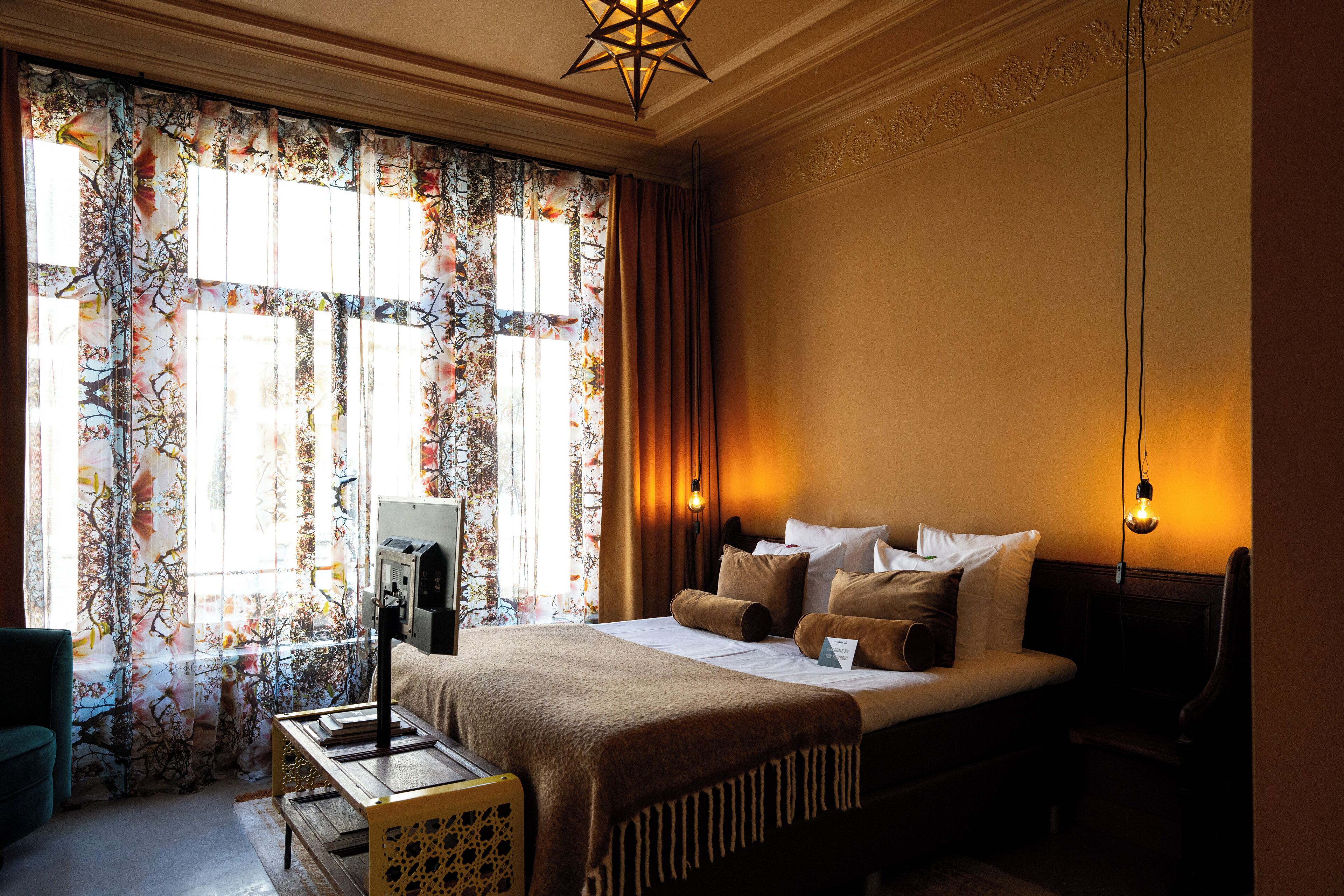 A hotel room with a bed, bedside table, lamp, and curtains.