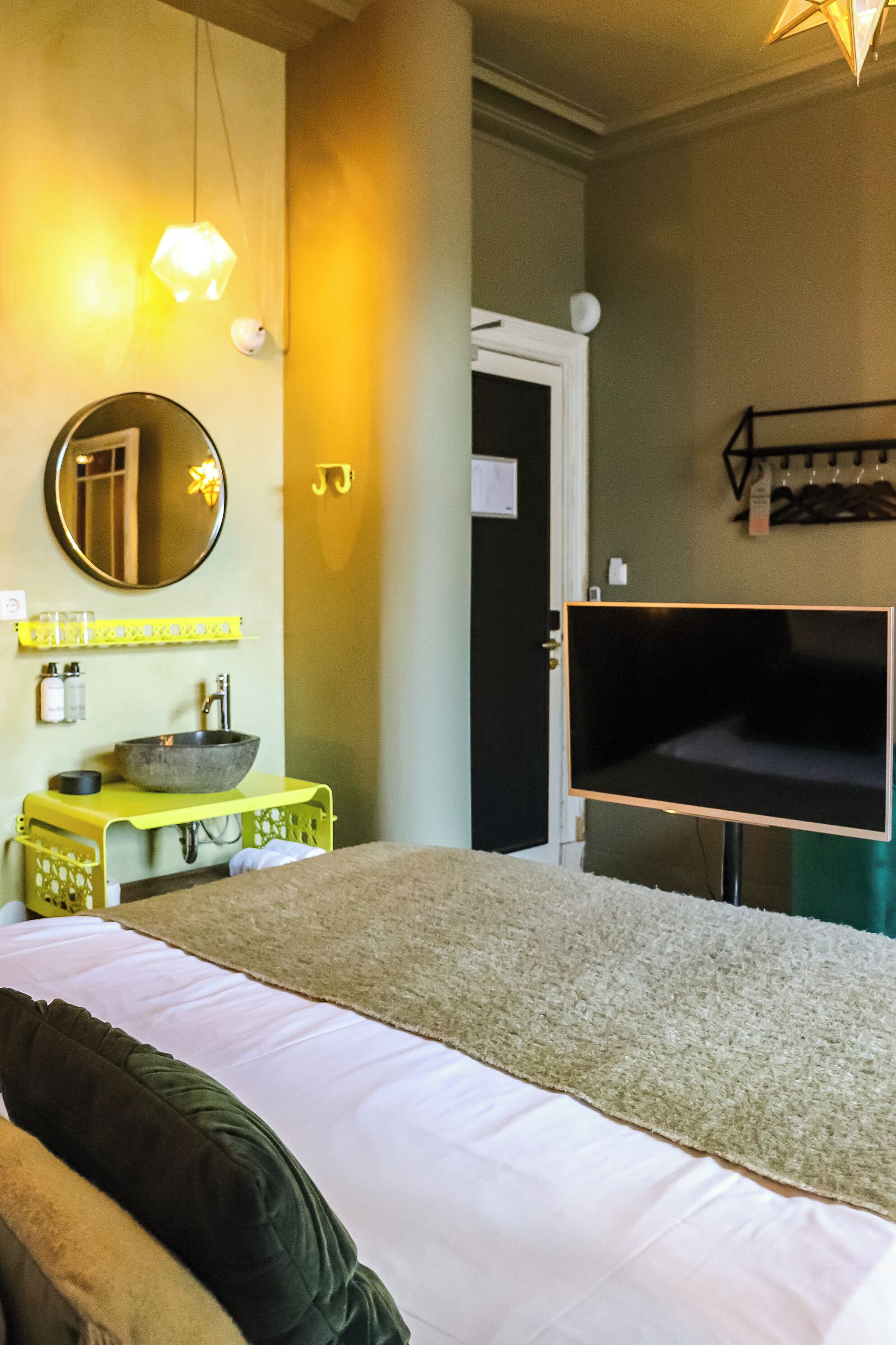 A hotel room with a bed, a TV, a sink, and a mirror.
