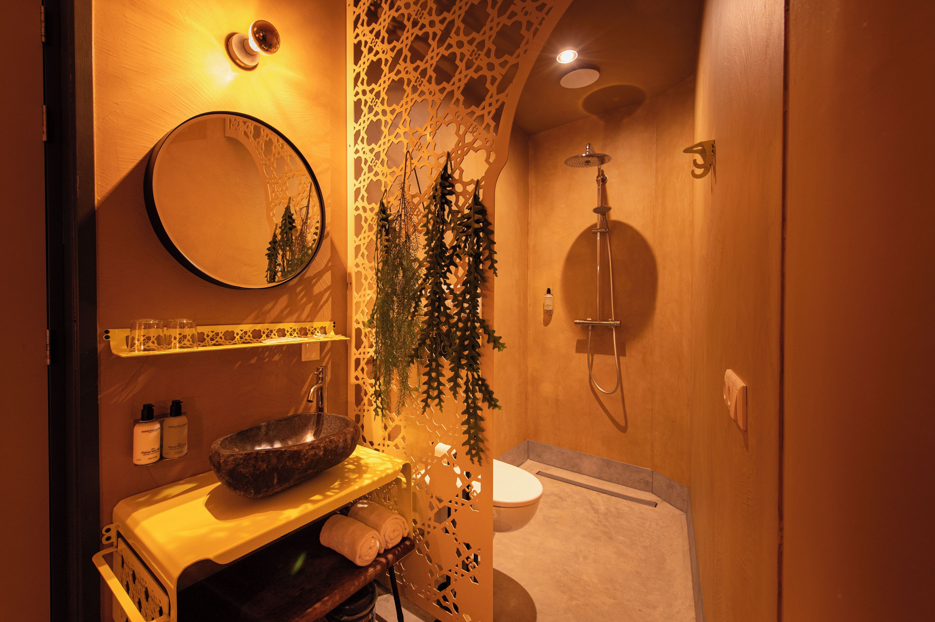 Un baño con tocador de madera, un espejo redondo, lavamanos con cuenca, inodoro y ducha.