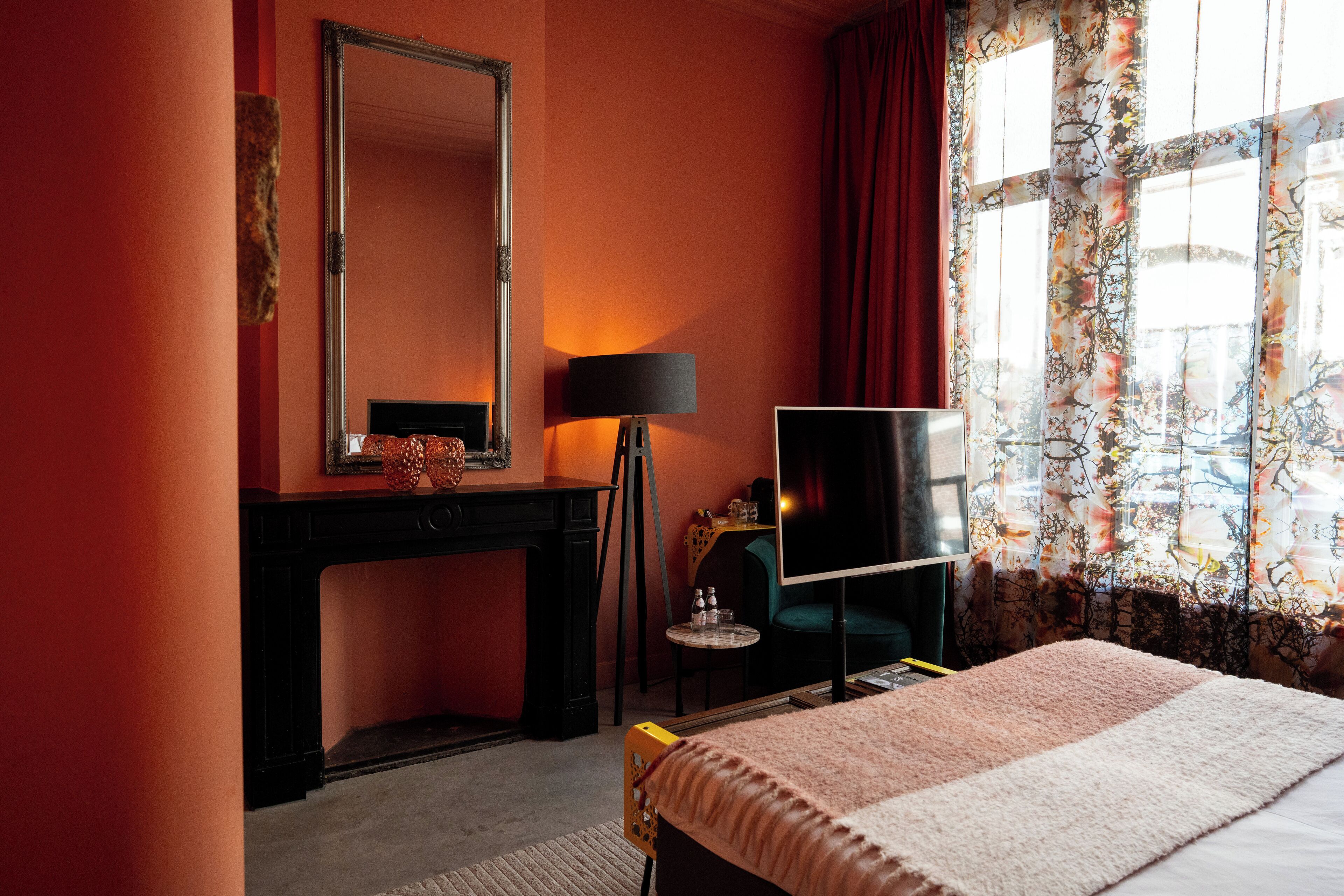 A hotel room with a large bed, a desk with a mirror, a television, and a window with curtains.