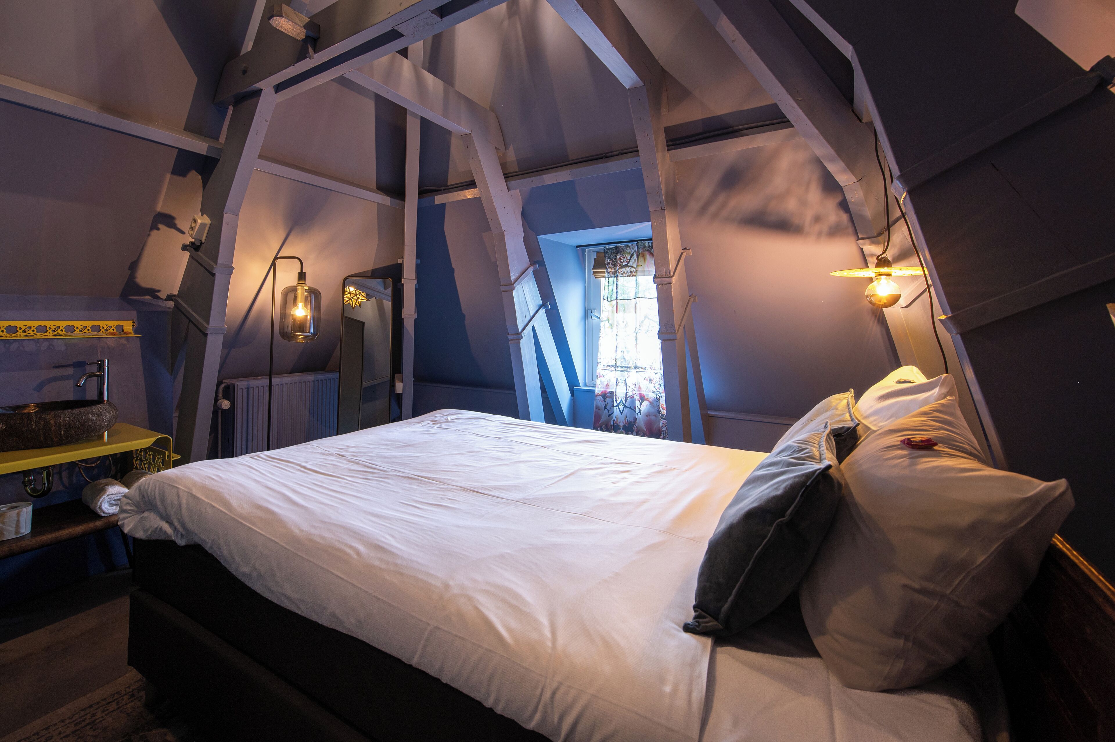 A bedroom with a bed, a nightstand, a window with curtains, and a wall-mounted light fixture.