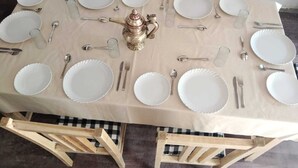 Una mesa de comedor dispuesta con platos blancos, cubiertos y una tetera de latón.