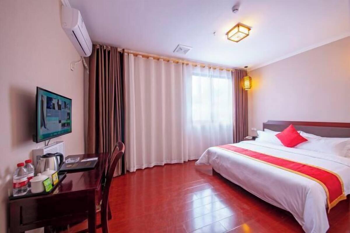A hotel room with a bed, a desk with a chair, a television, and a window with curtains.