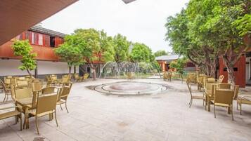 An outdoor seating area with tables and chairs, a fountain, and trees.