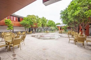 An outdoor seating area with tables and chairs, a fountain, and trees. - Yuzhong Baguo Hotel (Langzhong)