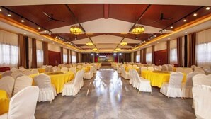 A banquet hall with rows of tables and chairs, a high ceiling with chandeliers, and a central stage area.