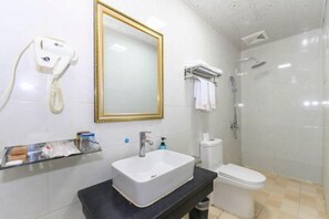 A bathroom with a white sink, a toilet, a shower, a gold-framed mirror, and a hairdryer on the wall. - Yuzhong Baguo Hotel (Langzhong)