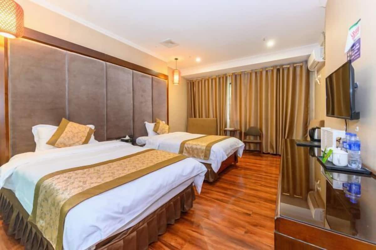 A hotel room with two beds, a large padded headboard, a television, and a minibar.