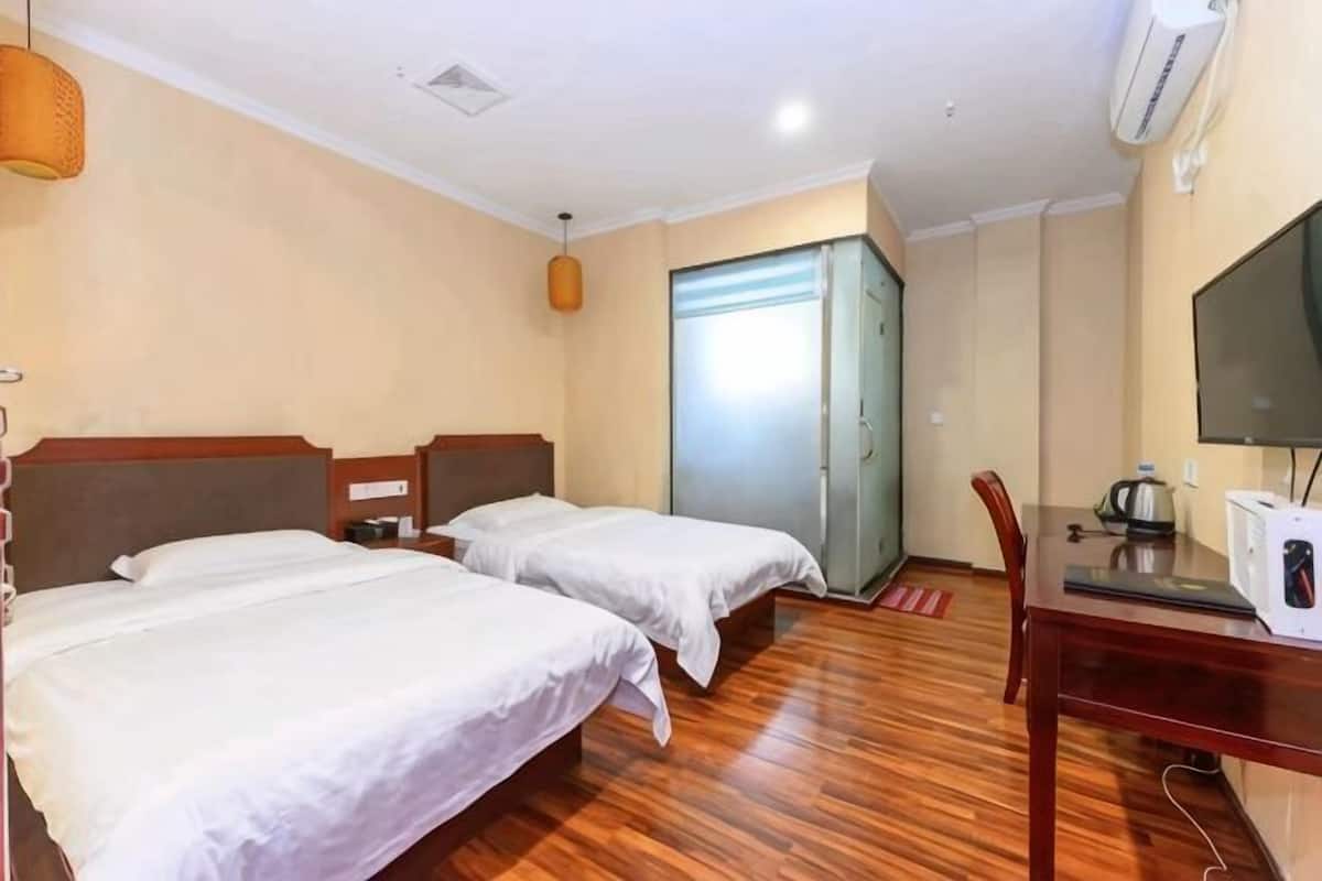 A hotel room with two beds, a wooden floor, a desk with a television, and a wardrobe.
