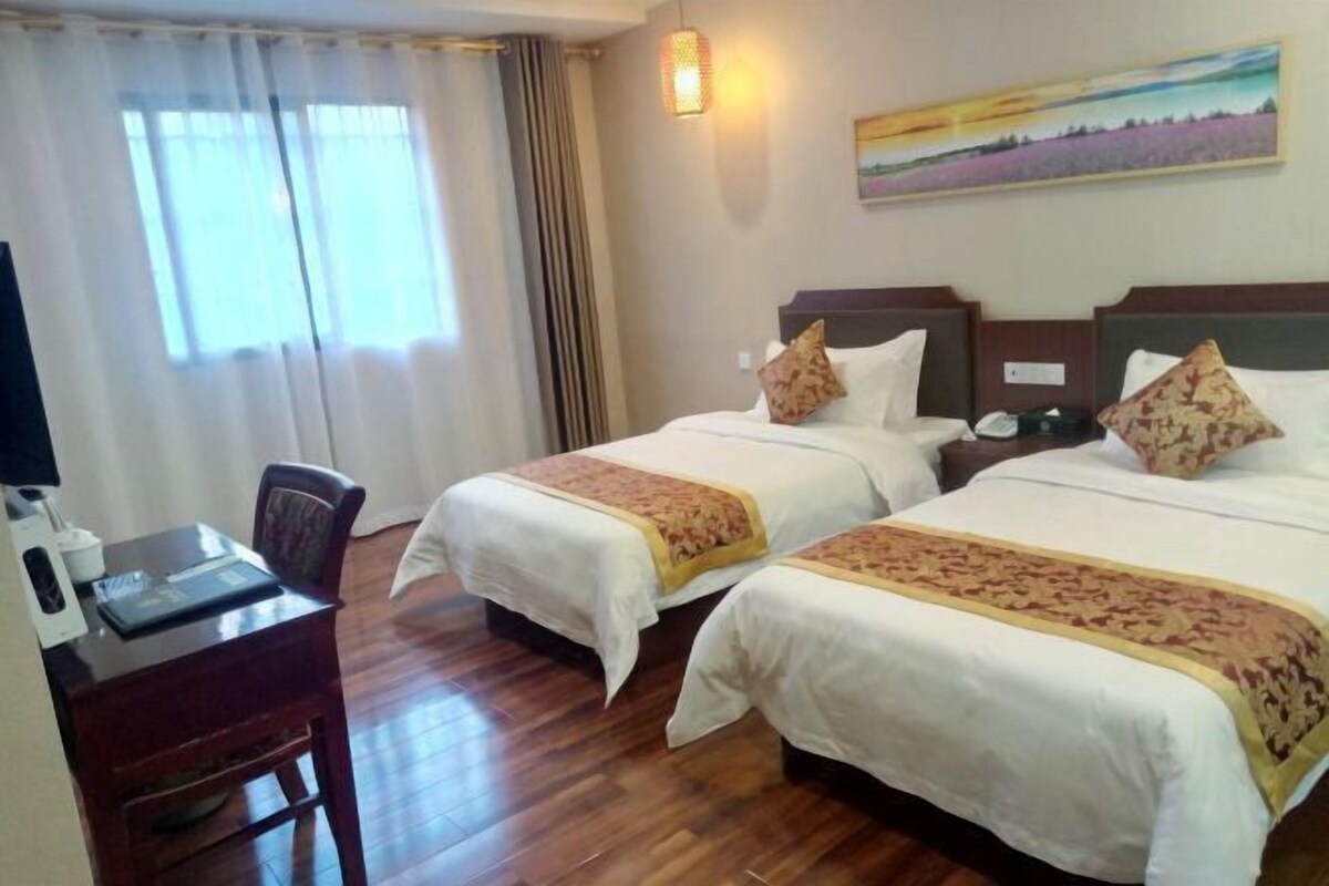 A hotel room with two beds, a desk, a chair, a lamp, and a painting on the wall.