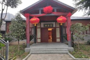 Un bâtiment traditionnel avec une entrée rouge, une enseigne indiquant « 华客厅 » et des lanternes rouges.