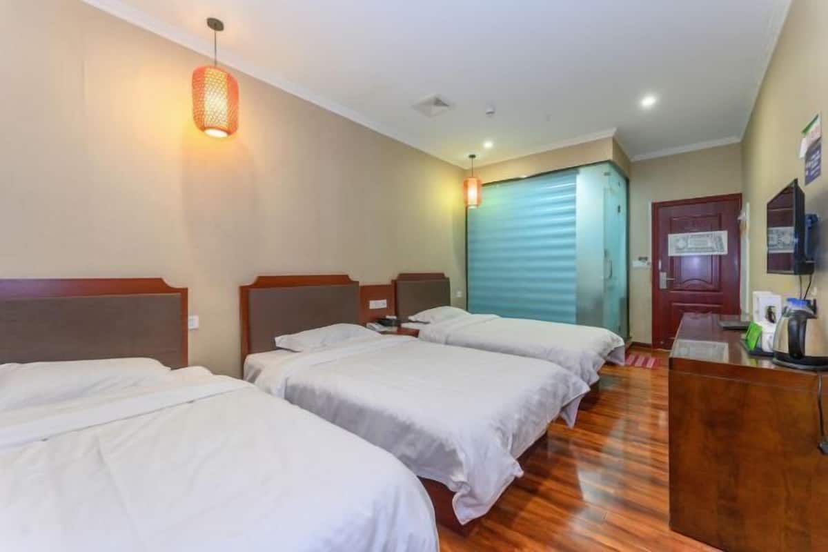 A hotel room with three beds, a wooden desk, and a closed door.