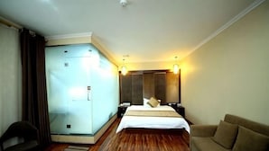 A hotel room with a bed, a sofa, a desk, and a glass partition.