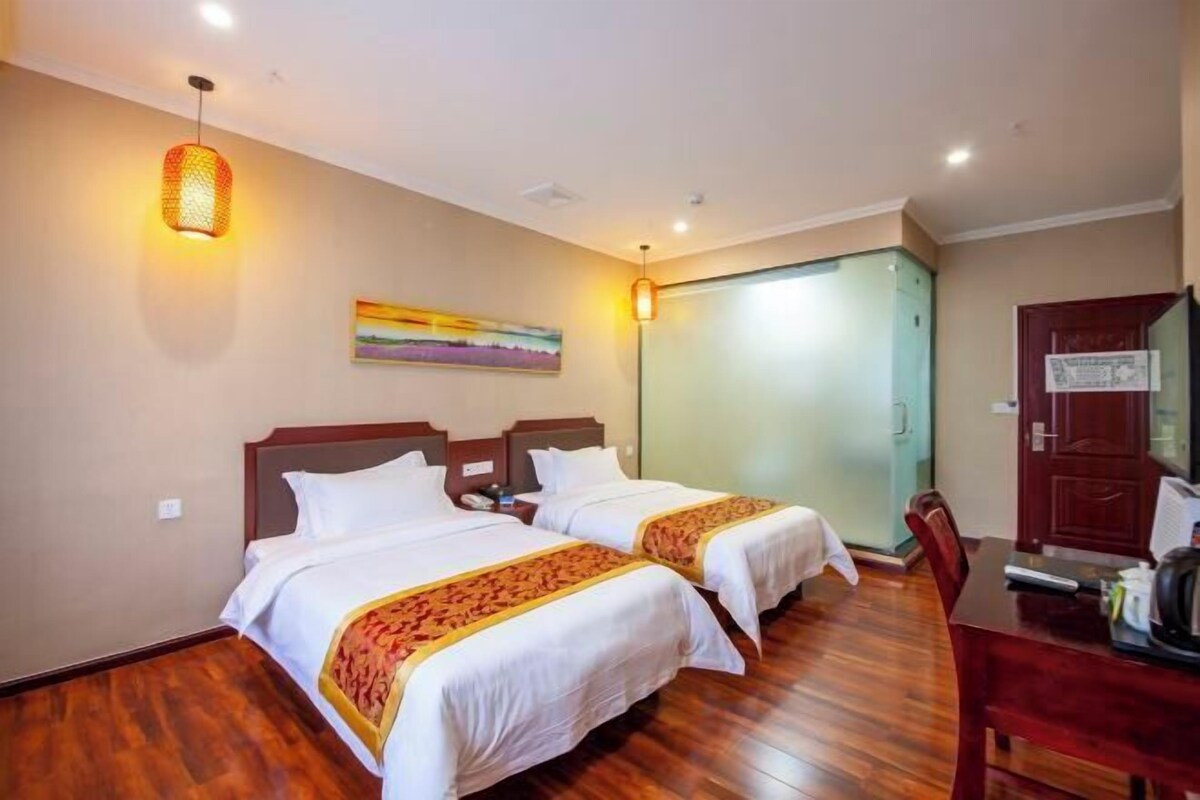 A hotel room with two beds, wooden flooring, a painting on the wall, and a desk with a chair.