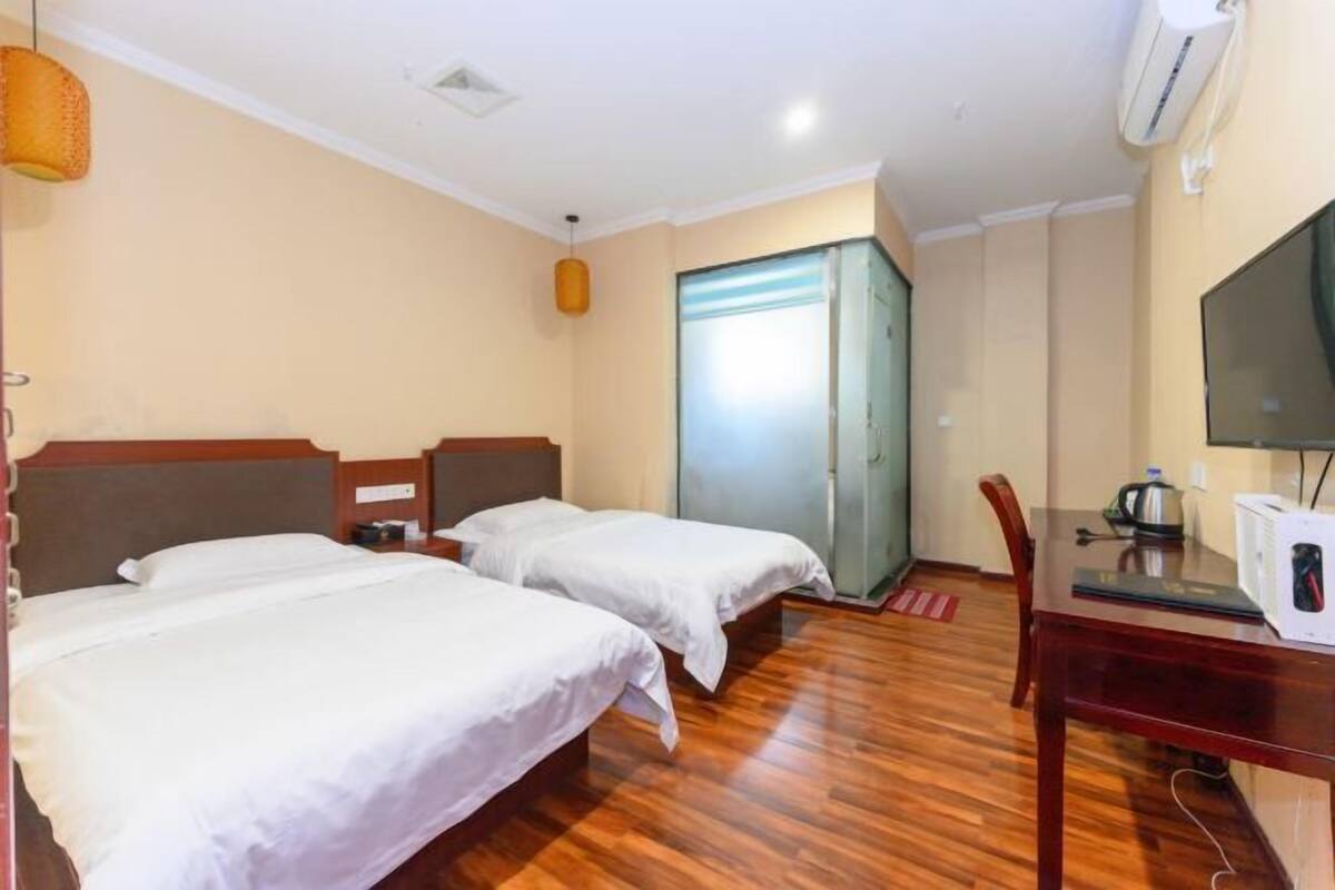 A hotel room with two beds, a wooden floor, a desk with a chair, a television, and a sliding door.