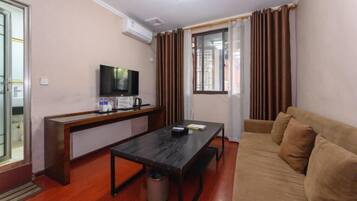 A compact living space with a sofa, a small table, a television, and a window with curtains.