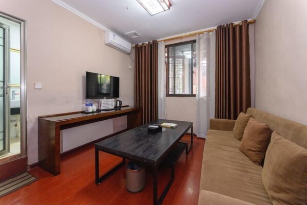 A compact living space with a sofa, a small table, a television, and a window with curtains. - Yuzhong Baguo Hotel (Langzhong)