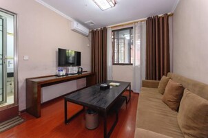 Un espacio habitable compacto con un sofá, una mesita, un televisor y una ventana con cortinas.