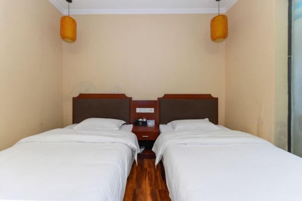 A hotel room with two single beds, wooden headboards, a nightstand, and two hanging lamps.