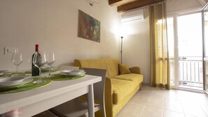 A dining area with a white table set for four, a yellow sofa, and a colorful abstract painting on the wall. - House IN HISTORIC CENTER with two double rooms ba (Castellammare del Golfo)
