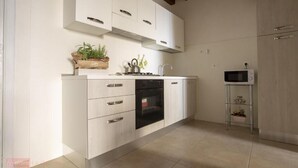 A modern kitchen with white cabinetry, a built-in oven, and a small island with a kettle. - House IN HISTORIC CENTER with two double rooms ba (Castellammare del Golfo)