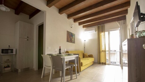 A dining area with a table set for two, a yellow sofa, and a kitchen with a microwave. - House IN HISTORIC CENTER with two double rooms ba (Castellammare del Golfo)