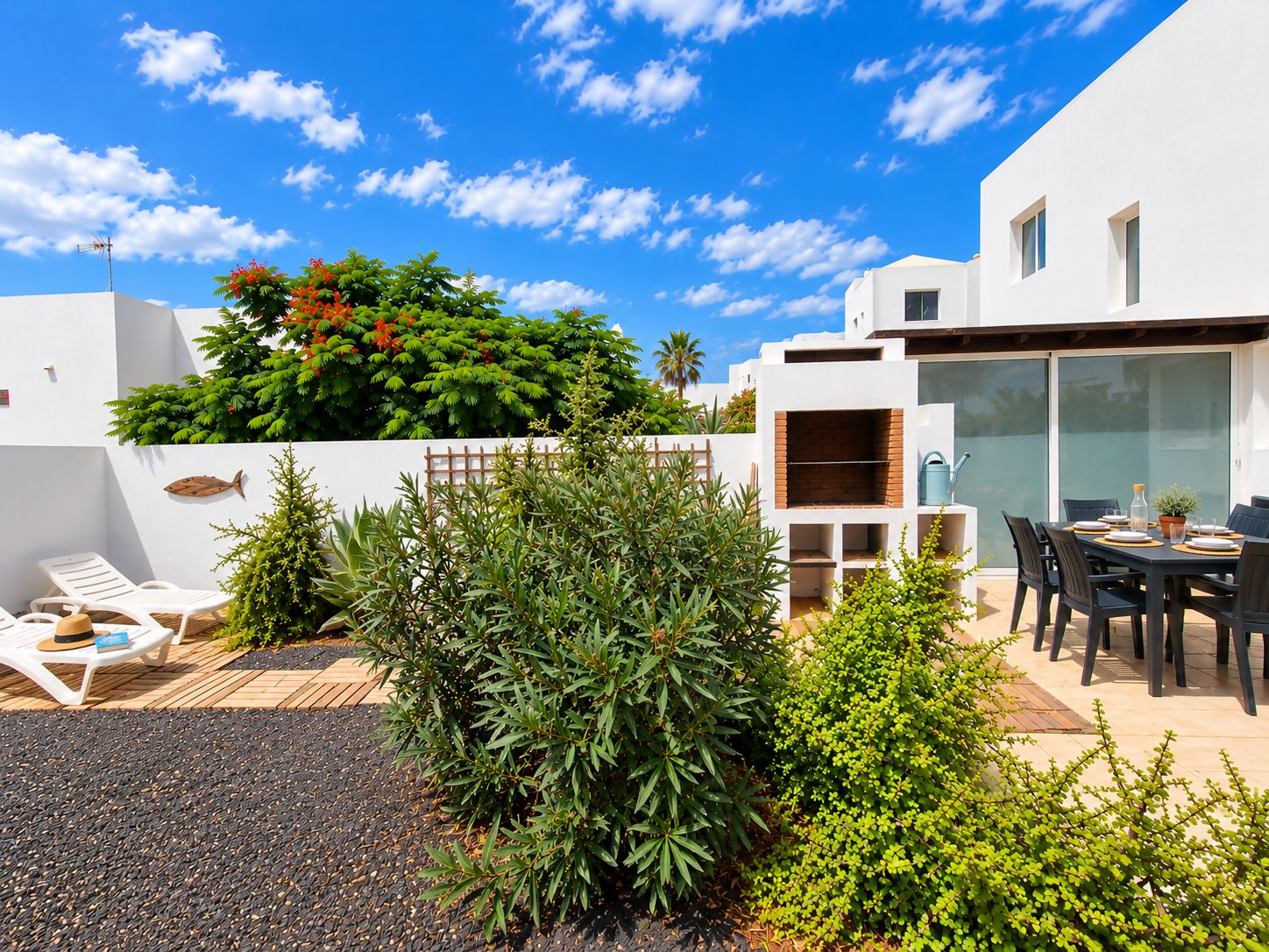 Une terrasse extérieure moderne, dotée d’une table et de chaises, entourée de différentes plantes et bordée d’un bâtiment blanc.