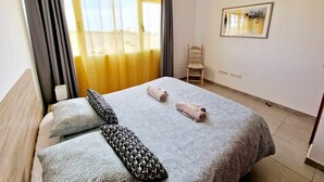 Une chambre d’hôtel avec un lit, deux oreillers, une chaise, un tableau au mur et une fenêtre avec des rideaux.