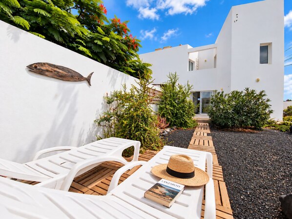 Un área de estar moderna al aire libre con sillones blancos, una terraza de madera y un libro titulado 'LANZAROTE' sobre una de las sillas.