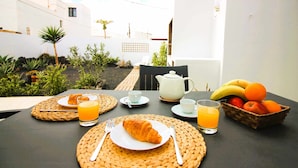 Une table dressée pour le petit-déjeuner, avec des croissants, du jus d’orange et un panier de fruits.