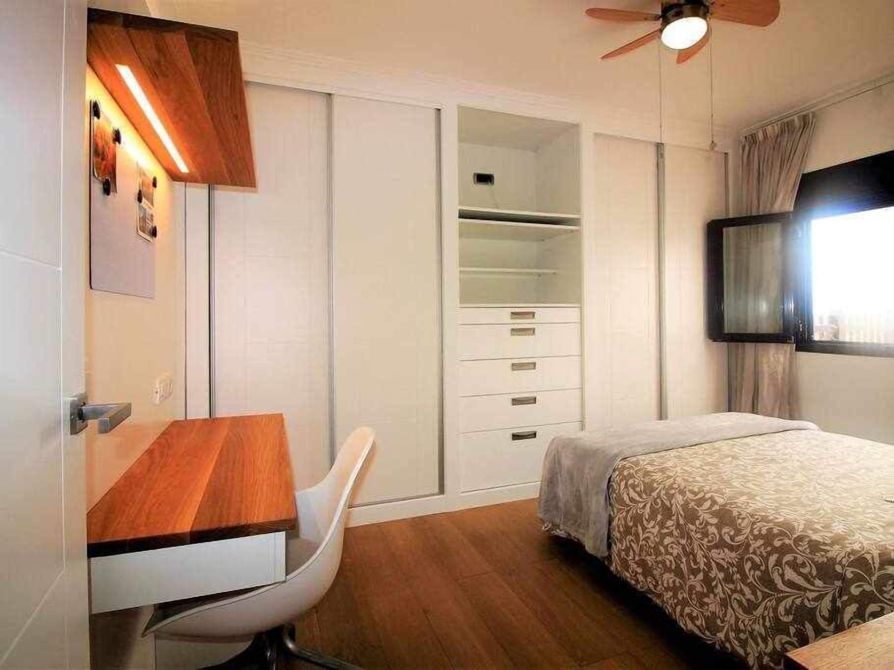 A bedroom with a bed, a desk, a chair, a wardrobe, and a ceiling fan.