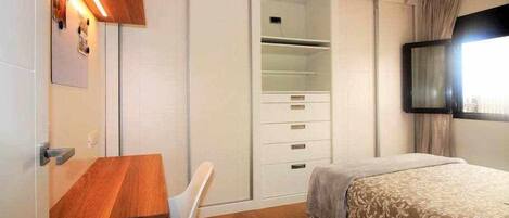 A bedroom with a bed, a desk, a chair, a wardrobe, and a ceiling fan.