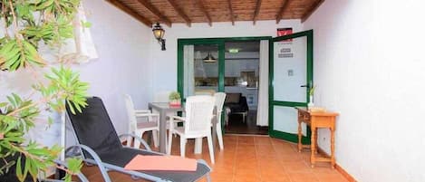 A small patio area with two lounge chairs, a table, and a door leading to a kitchen.
