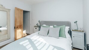 Een slaapkamer met een bed, nachtkastjes, een dressoir en een deur.