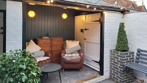 Een gezellig buiten zitgedeelte met een houten stoel en een kleine tafel, een witte bakstenen muur en een deur naar een garage.