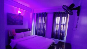 Una habitación con cama, escritorio, ventilador de pared y cortinas.