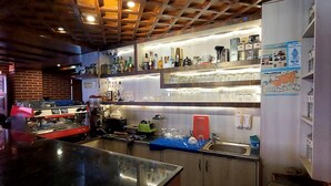 Zona de bar con mostrador, estanterías con botellas, vasos y un mapa en la pared.