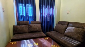 Una sala de estar con un sofá marrón, una mesa de centro de madera con diseño floral y una ventana con cortinas azules.