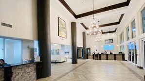 Eine geräumige Lobby mit Fischgrätparkett, großen Säulen, einem Empfangsbereich und einer Kronleuchter.