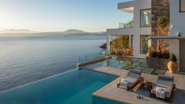 Une maison moderne dotée d’une piscine à débordement en verre, offrant une vue imprenable sur une mer calme.