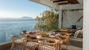 Un coin repas avec vue sur la mer, des meubles en bois et une table dressée avec de la nourriture et des boissons.