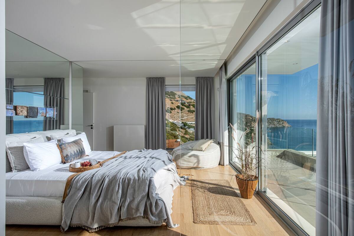 Ein modernes Schlafzimmer mit einem großen Bett, einem Sitzsack, einer Topfpflanze und Meerblick.