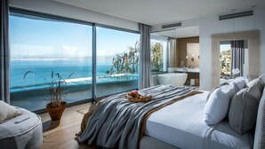 Une chambre moderne avec une grande fenêtre, un lit, une table de chevet et une vue sur la mer.
