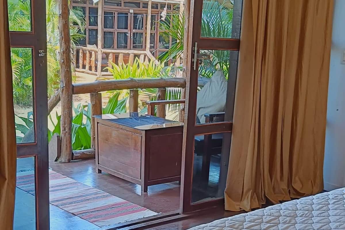 A room with a bed, a sliding glass door leading to an outdoor area with a wooden deck and a building.